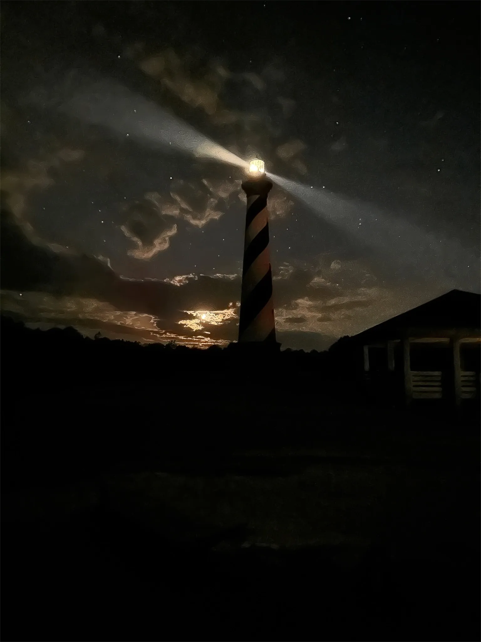 The Cape Hatteras lighthouse at night, its beams sweeping across a starry sky and moonlit clouds
