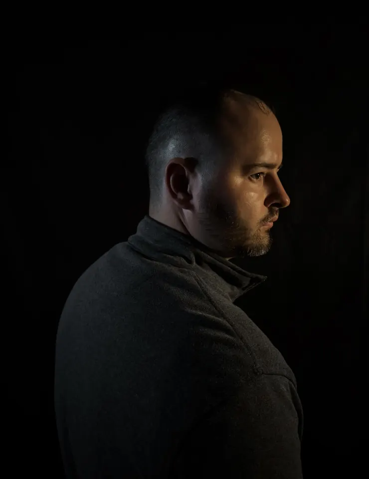 Christian in profile, lit from the side against a black background