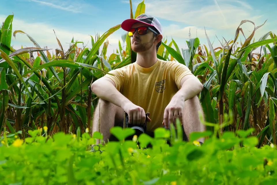 A young man in a cap sitting among tall corn on a sunny day
