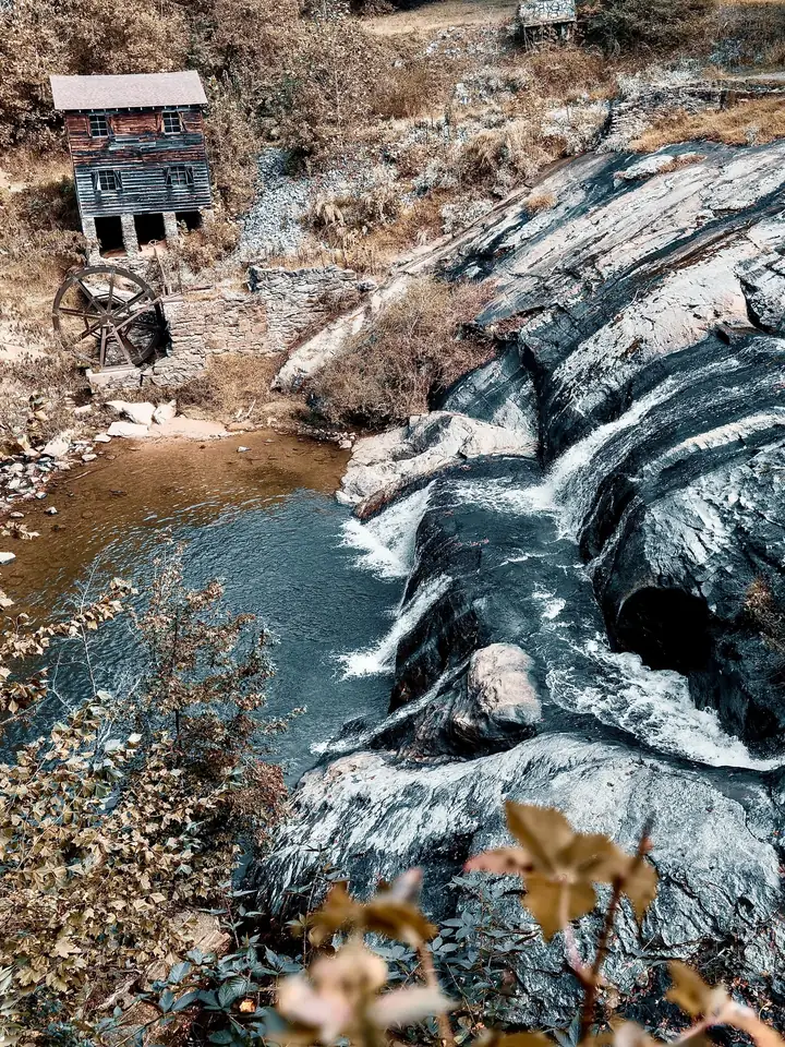 Water pouring over dark rock ledges below an old mill at McGalliard Falls