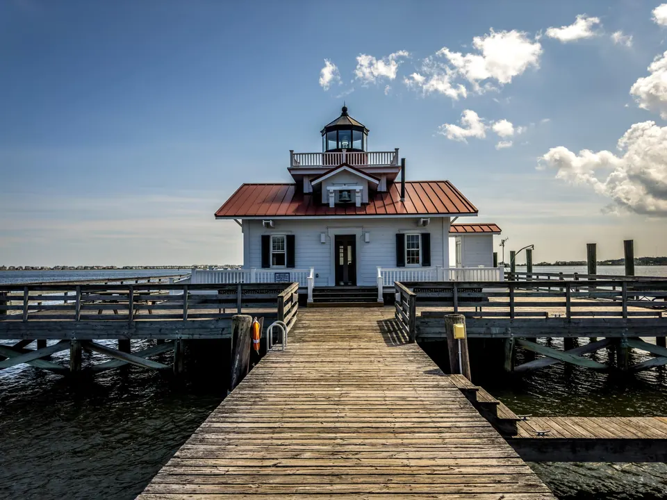 Roanoke Marshes Lighthouse, a white cottage-style lighthouse at the end of a long wooden pier