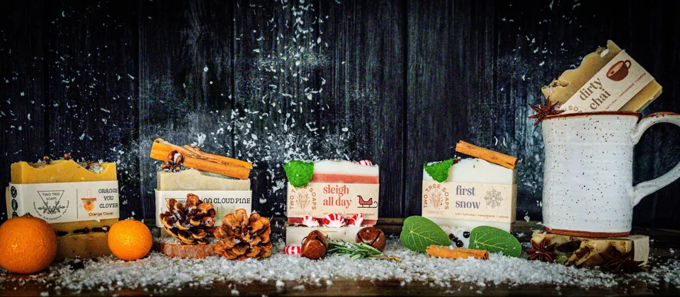 Soaps lined up on a dark wooden surface with oranges and pinecones