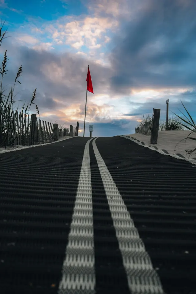 A boardwalk path climbing over the dunes toward the beach at dusk, a red flag flying