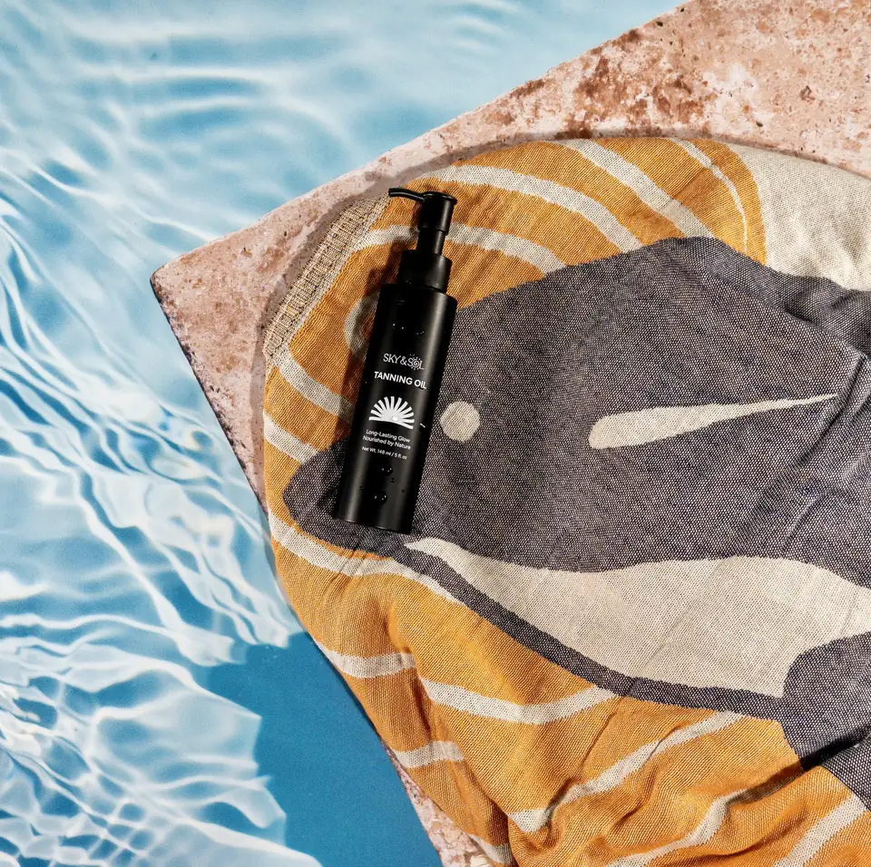 A bottle of Sky and Sol tanning oil on a striped towel beside a pool