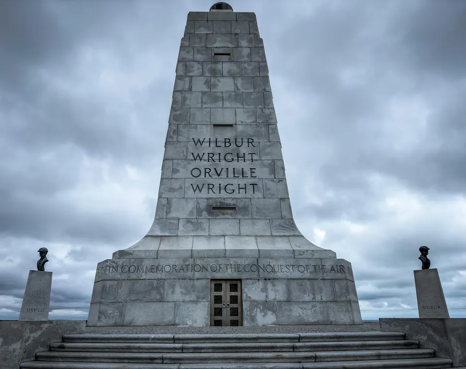 The granite Wright Brothers monument under a heavy gray sky